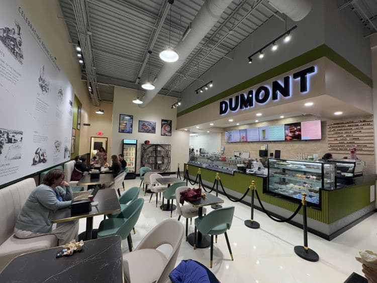 Interior view of a bustling DUMONT cafe with patrons, tables, and a green counter.